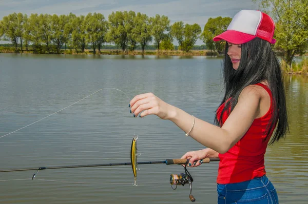 Joven pescadora preparándose para la pesca. Chica con caña de pescar mira señuelo —  Fotos de Stock