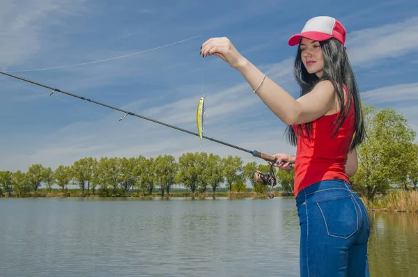 Young fisherwoman preparing for fishing. Girl with fishing rod looks at lure — Stock Photo, Image