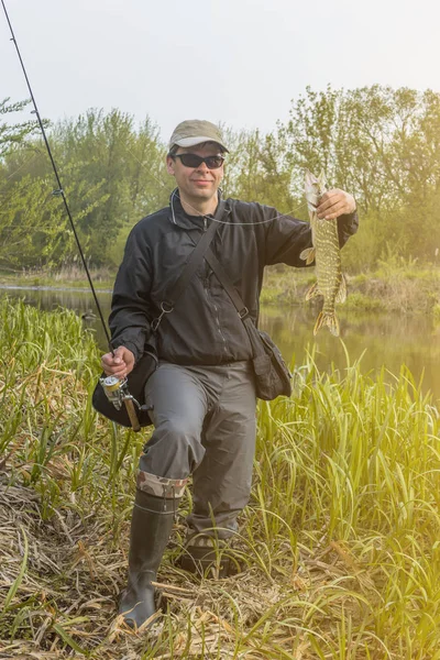 Fischerei. glücklicher Fischer mit Hechtfischtrophäe und Angelrute am Fluss — Stockfoto