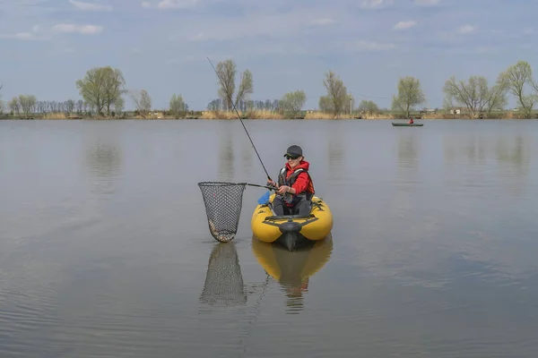 Kayak fishing at lake. Fisherwoman with pike fish on inflatable boat with fishing tackle.