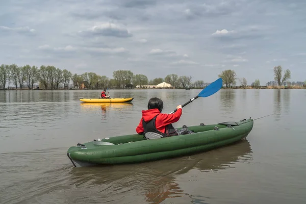 Kayak fishing at lake. Two fisherwomen on inflatable boats with fishing tackle.