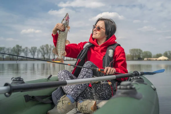 Kajak horgászat. Halász lány gazdaság csuka hal trófeát a felfújható csónak horgászfelszerelés tónál. — Stock Fotó