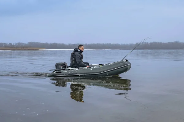 Łowienie ryb. Rybak na nadmuchiwanej łodzi z sprzętem wędkarskim na jeziorze w zimie. — Zdjęcie stockowe