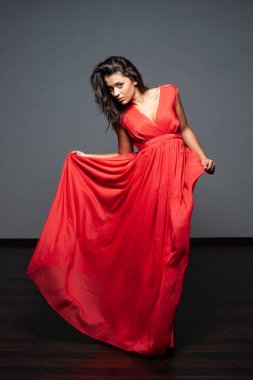 Genç ve güzel seksi model erkek şaşırtıcı uzun kırmızı elbise ve siyah ayakkabı karanlık Studio'da poz koyu saçlı