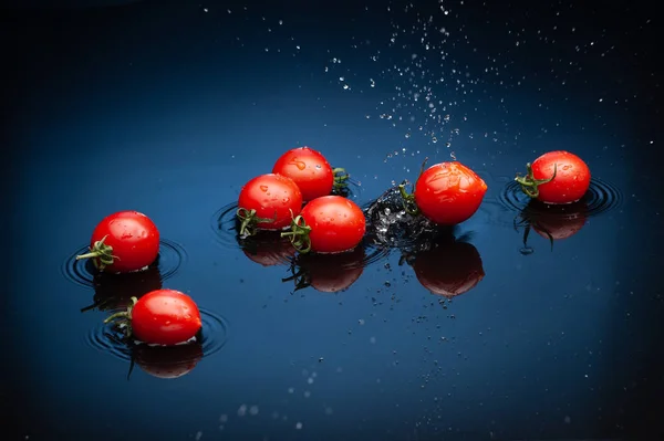 Tomates em um fundo de espelho preto no respingo de água . — Fotografia de Stock