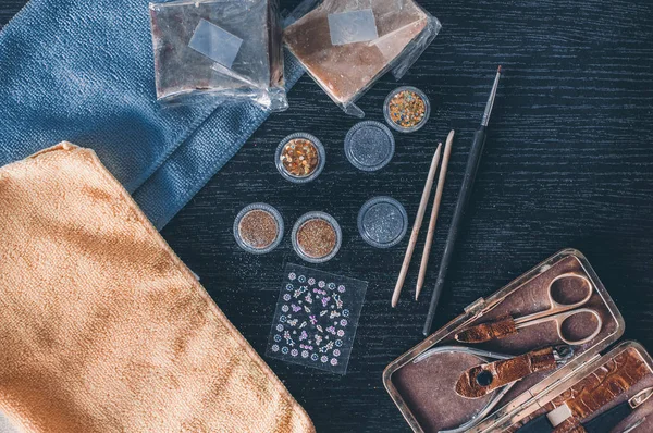 Flat lay of nail polishes and colorful towels. Bright gold and silver tinsel, brush for nails, manicure set of scissors, tweezers and nail stickers