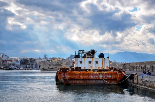 Heraklion, Crete - Greece. Floating Crane at the port of Heraklion. Fortress Koules and part of Heraklion at the background. Sun rays breaking through the clouds of a dramatic sky over the city