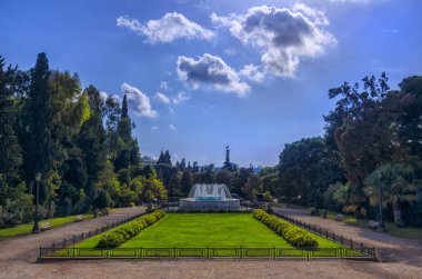 Atina, Attica / Yunanistan. Syntagma Meydanı yakınındaki Ulusal Bahçe Zappeion Hall neo-klasik binanın önünde mermer çeşme ile bahçe. Güneşli bir gün, bulutlu gökyüzü, kimse