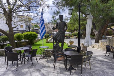 Archanes, Girit Adası / Yunanistan. Geleneksel kahve dükkanları ile Archanes köyümerkez Meydanı. Osmanlı İmparatorluğu'na karşı savaşan Giritli kahramanın bronz heykeli