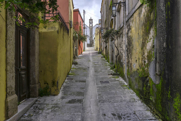Archanes, Crete Island / Greece. Narrow paved alley, in Archanes village that leads to a church, with old traditional houses with moss on their walls