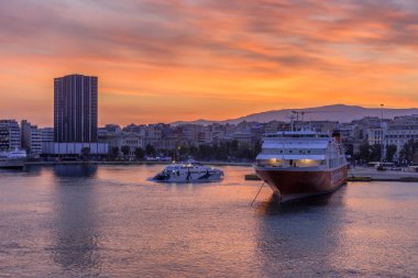 Pire Limanı, Attica / Yunanistan. Liman ve Pire şehri üzerinde ateşli gökyüzü ile renkli gündoğumu. İskeleye demirlemiş yolcu gemileri