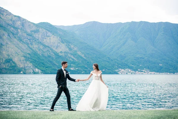 Casamento Casal Correndo Longo Grama Contra Fundo Lago Montanhas — Fotografia de Stock