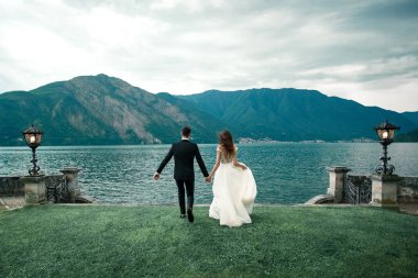 Düğün çifti çimen göl ve dağların arka planı boyunca çalışan