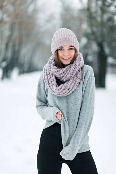 Hermosa chica sonriente se para en el camino en un sombrero y suéter en el invierno —  Fotos de Stock