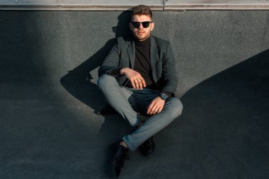 mutlu genç adam koruyucu gözlük ve gri arka plan üzerinde gri bir takım oturuyor. güneşli gün.