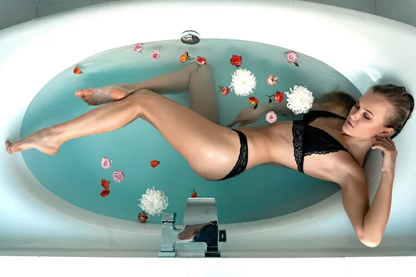Красивая молодая девушка в ванной комнате с водой и розы в черном белье — стоковое фото