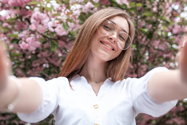 Bela jovem mulher feliz em uma blusa e óculos perto das flores de cereja — Fotografia de Stock