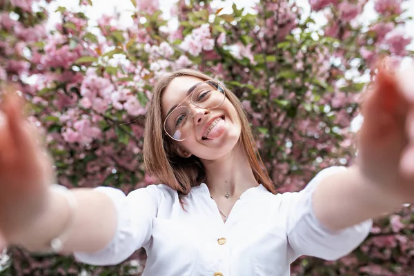 Bela jovem mulher feliz em uma blusa e óculos perto das flores de cereja — Fotografia de Stock