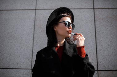 Şapkalı güzel genç bir kadın dudaklarını boyuyor.