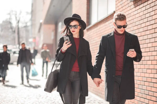 Чоловік і жінка в чорному йдуть і дивіться на телефон — стокове фото