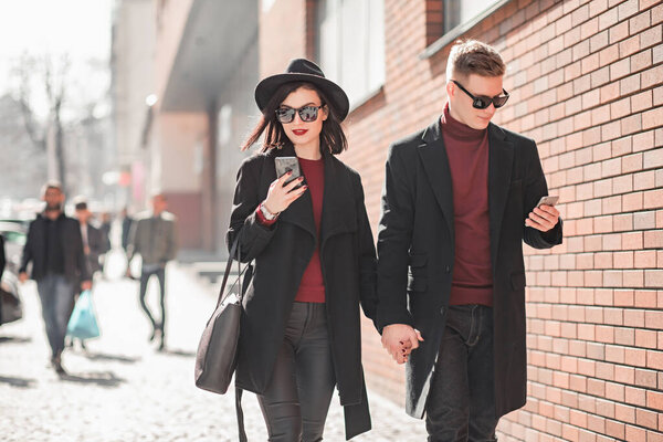 мужчина и женщина в черном идут и смотрят на телефон
