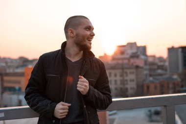 Genç yakışıklı adam şehrin arka planında gün batımını seyrediyor.