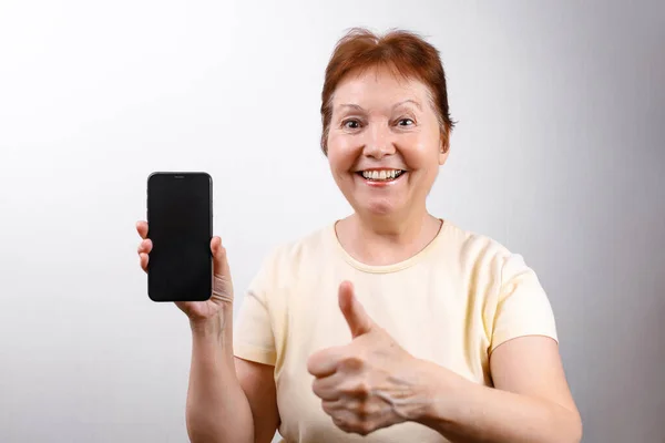 Mujer Mayor Muestra Teléfono Sobre Fondo Blanco Una Camiseta Ligera —  Fotos de Stock