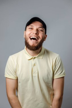 Sarı tişörtlü ve siyah şapkalı mutlu bir gencin portresi gri arka planda başka yere bakıyor. İzole. Kopyalama alanı