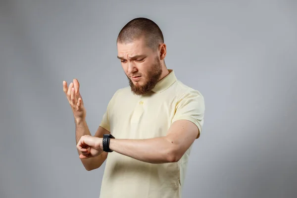 Porträtt Ung Man Gul Shirt Tittar Hans Klocka Grå Bakgrund — Stockfoto