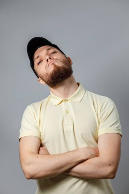 Sarı tişörtlü, siyah şapkalı, gri arkaplanlı ciddi bir gencin portresi. İzole. Kopyalama alanı