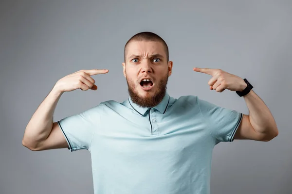 Retrato de um jovem em uma camiseta azul com raiva gritando sobre um fundo cinza. isolado — Fotografia de Stock