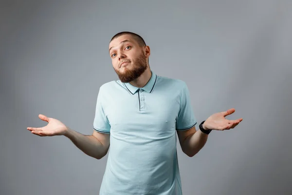 Porträt eines jungen Mannes in einem blauen T-Shirt, der ratlos vor grauem Hintergrund steht. Vereinzelt. Kein Geld Stockbild