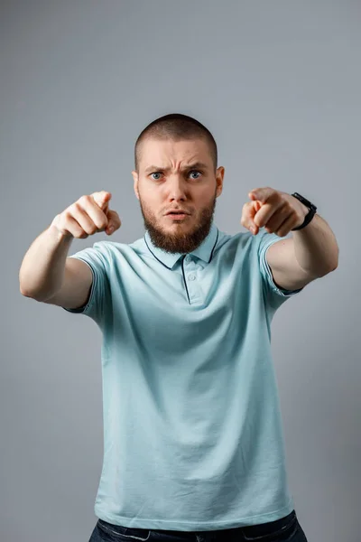 Retrato de um jovem em uma camiseta azul com raiva gritando sobre um fundo cinza. isolado — Fotografia de Stock