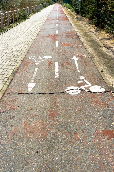 Closed and broken bike lane with worn out bike symbols in both directions. A crack goues from left to right in the pavement and the red color is barely visible anymore