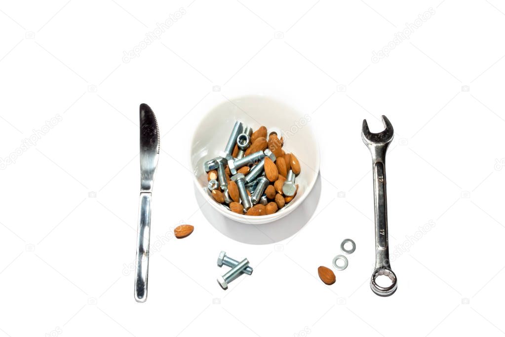 Cereal bowl filled with hard to digest almonds, nuts and bolts with a knife and a spanner lying next to it, isolated on white background