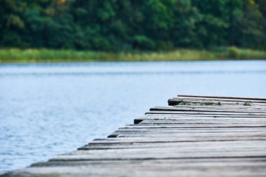 Çapraz olarak göl ve kıyı arka planda görünür karede çalıştıran bir ahşap iskele tarafında closeup.