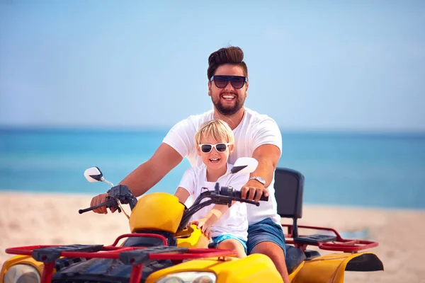 Счастливая семья, отец и сын катаются на квадроцикле на песчаном пляже — стоковое фото