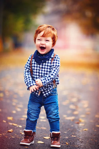 可爱的红头发蹒跚学步的小男孩在秋街落叶中漫步 — 图库照片
