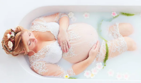 美丽的年轻孕妇放松在牛奶浴手在腹部 嫩产妇 — 图库照片