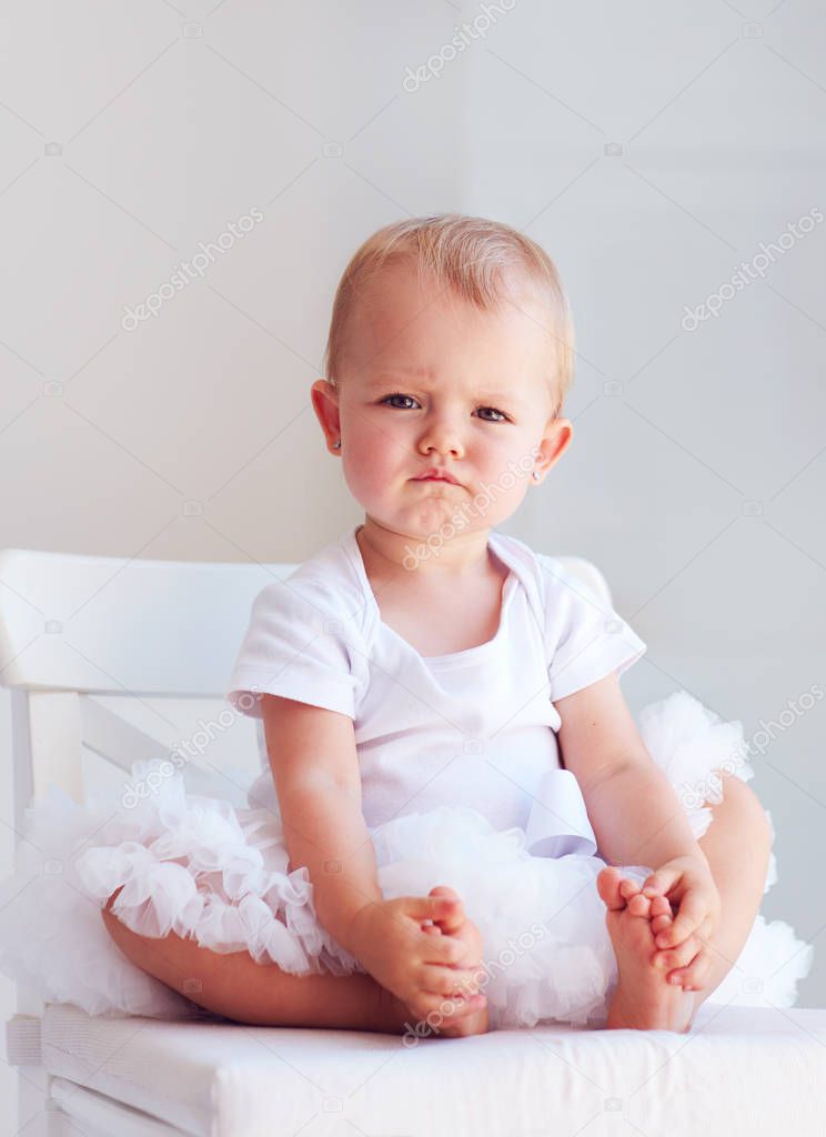 portrait of one year old baby girl with serious face expression and fiery temper posing on the chair