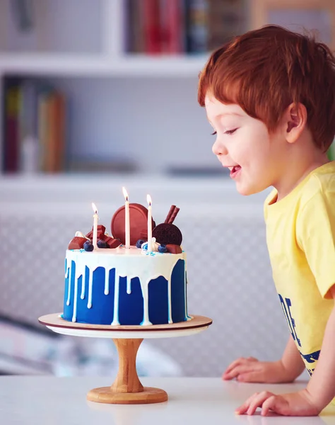 Söt rödhårig lycklig pojke, Kid blåser ljus på födelsedagstårta på sin tredje födelsedag — Stockfoto