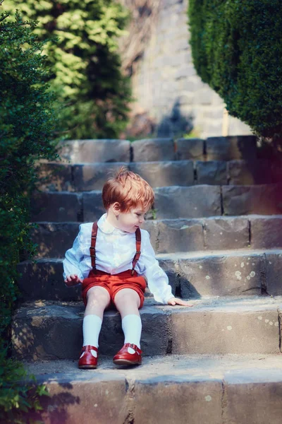 Carino rossa bambino seduto su trairs in primavera giardino — Foto Stock