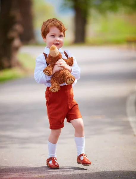 Mignon rousse bébé garçon avec peluche ours marche dans le parc de printemps — Photo