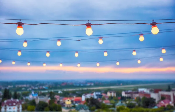 Несколько рядов декоративных наружных световых струн, висящих на фоне городского пейзажа в сумерках — стоковое фото