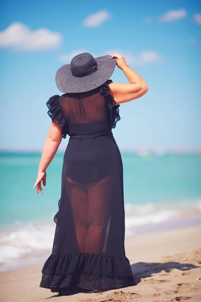 Beautiful plus size adult woman enjoys summer vacation by walking along the sandy beach — Stock Photo, Image