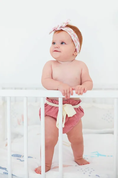 Funny, seven month old baby girl standing in her bed — Stock Photo, Image