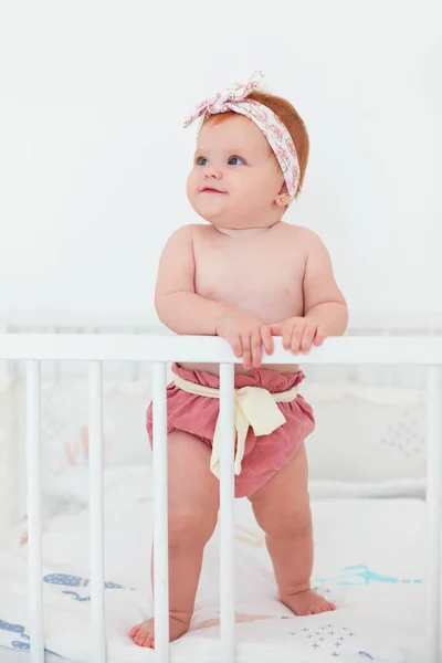 Divertida, niña de siete meses de pie en su cama —  Fotos de Stock