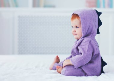 güzel gülümseyerek, dokuz aylık, dinozor kostümlü bebek kız, yatakta oturuyor