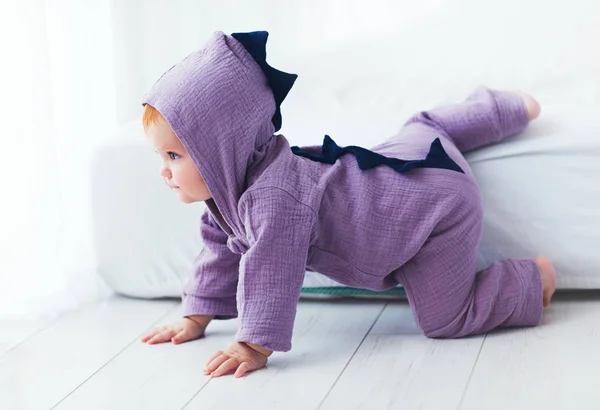 Grappig, negen maanden oud, zuigeling baby meisje in dinosaurus kostuum, naar beneden van het bed — Stockfoto