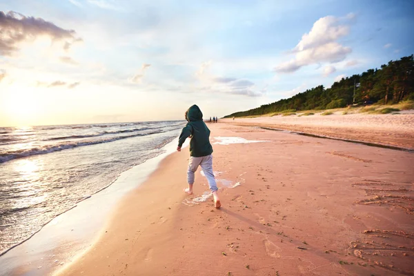 Cute young boy, kid having fun, running on the sandy autumn beach near the pine tree forest — Stock Photo, Image